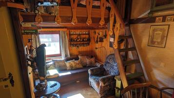 Un interior de madera acogedor con un sofá, sillas, una mesa con ruedas y una escalera.