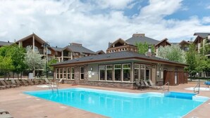 A pool area with lounge chairs and a building with large windows. - Lakeside Mountain Retreat - 3br, 2 bathroom beachfront condo with pool & hot tub (Invermere)