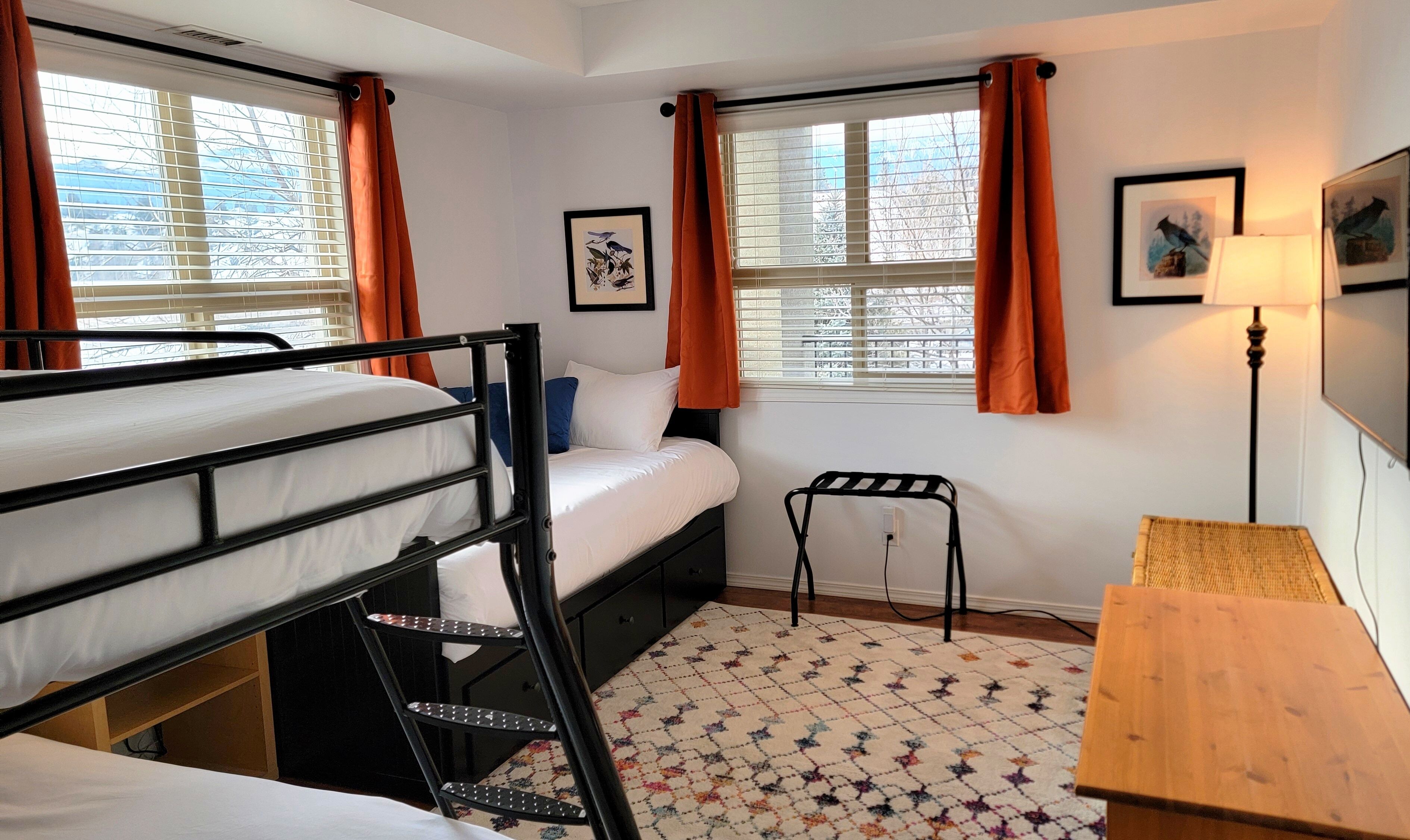 Une chambre de dortoir avec des lits superposés, un bureau, une chaise et deux fenêtres avec des rideaux.