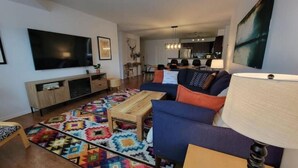A modern living room with a large flat-screen TV, a sofa, a coffee table, and a colorful rug. - Lakeside Mountain Retreat - 3br, 2 bathroom beachfront condo with pool & hot tub (Invermere)