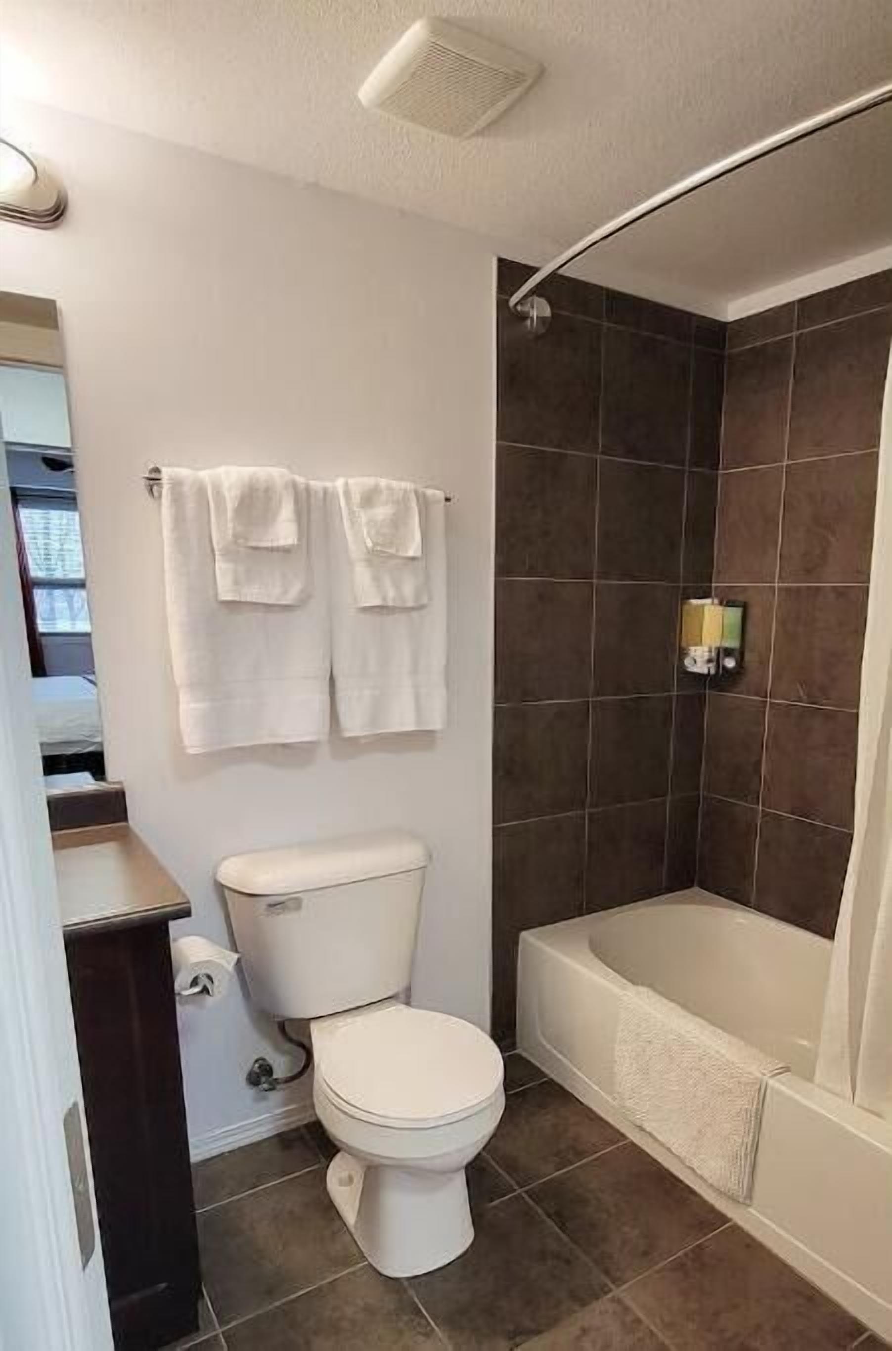 Un baño moderno con inodoro, ducha y bañera. Dos toallas cuelgan de la pared.