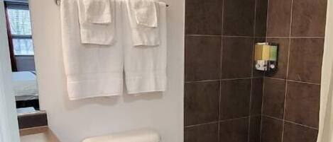 Un baño moderno con inodoro, ducha y bañera. Dos toallas cuelgan de la pared.
