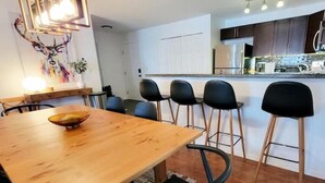 A modern kitchen with dark cabinets, a wooden dining table, and black bar stools. - Lakeside Mountain Retreat - 3br, 2 bathroom beachfront condo with pool & hot tub (Invermere)