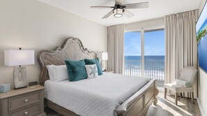 A bedroom with a large bed, a ceiling fan, a nightstand with a lamp, a chair, and a view of the ocean. - Majestic Sun A404*Remodeled*Gulf Views*HeatedPools*Hot Tubs*Beach Gears (Miramar Beach)