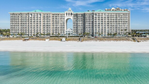 A large hotel with a central archway, located on a beach with clear turquoise water. - Majestic Sun A404*Remodeled*Gulf Views*HeatedPools*Hot Tubs*Beach Gears (Miramar Beach)