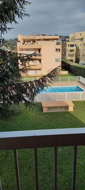 A residential building with a swimming pool, surrounded by greenery and a white fence.