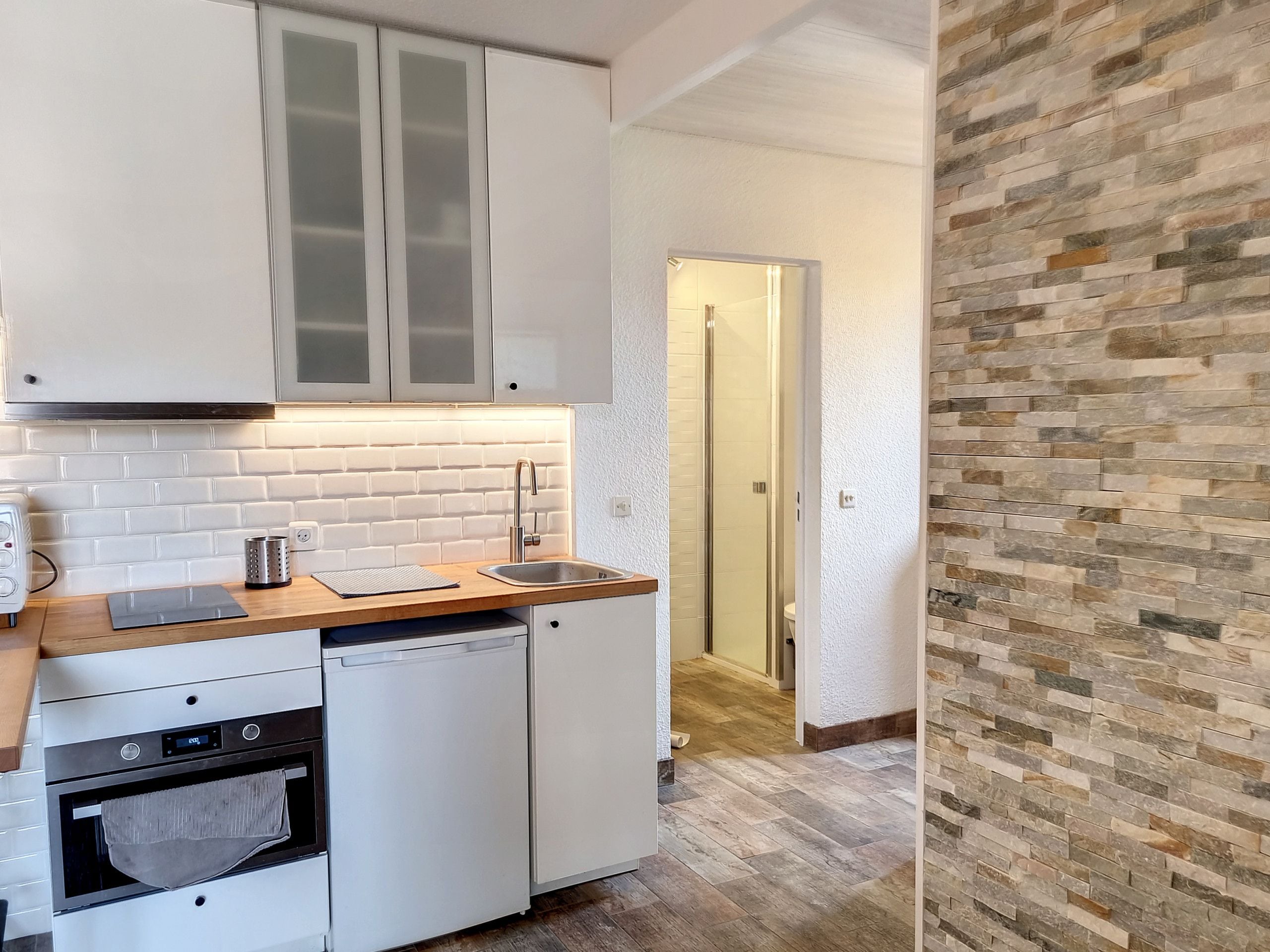 A compact kitchen with white cabinets, a built-in oven, and a dishwasher.