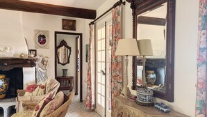 A traditional room with a fireplace, wicker furniture, a mirror, and a floral curtain. - VILLA LE MAS DE LA FORGE (Le Plan-de-la-Tour)