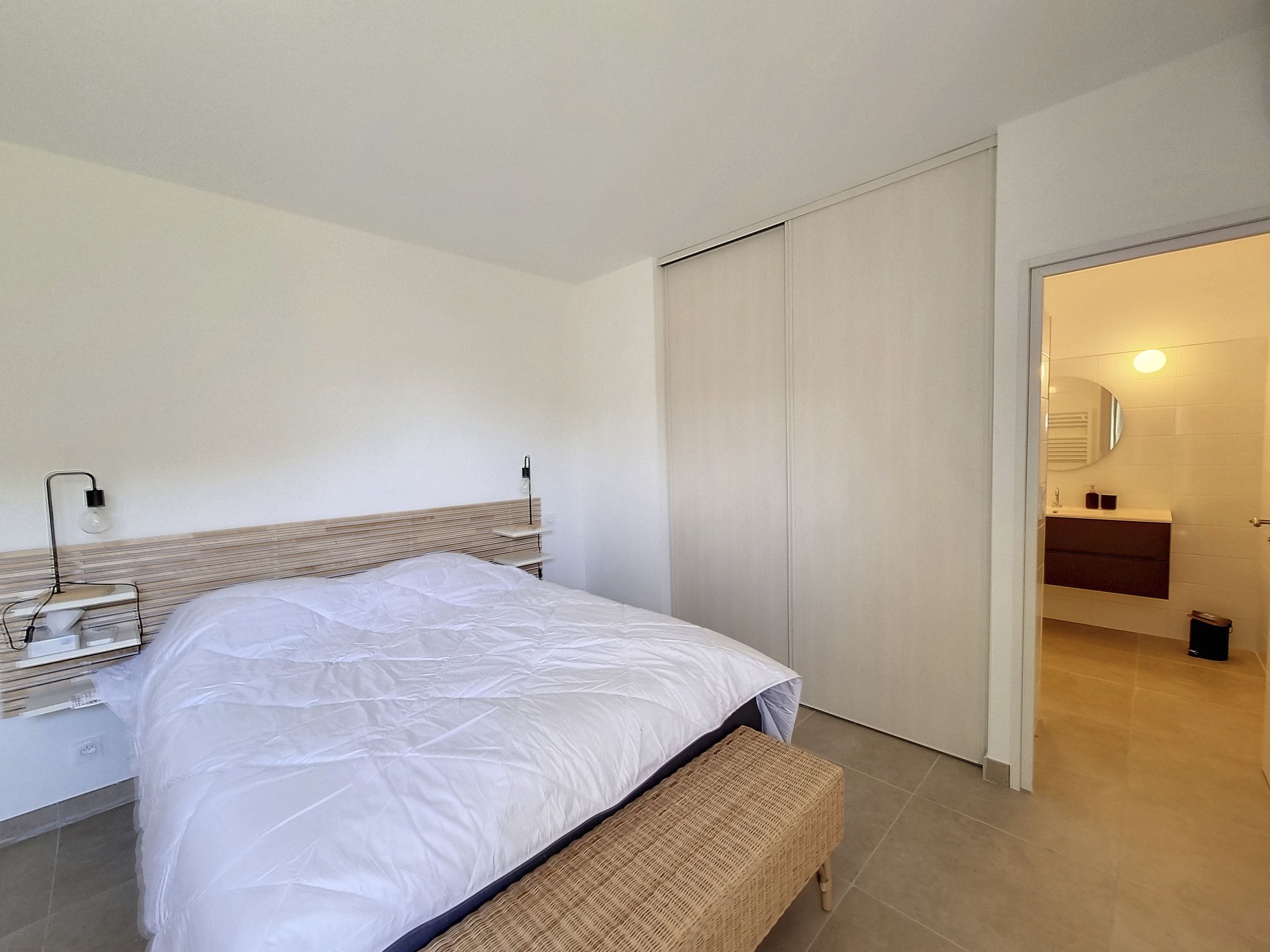 A modern bedroom with a bed, bedside table, lamp, and a bench.