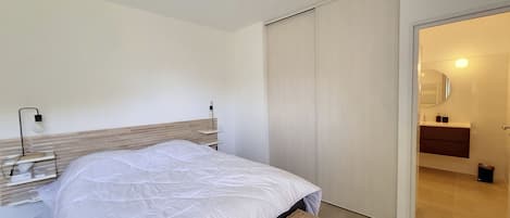 A modern bedroom with a bed, bedside table, lamp, and a bench.