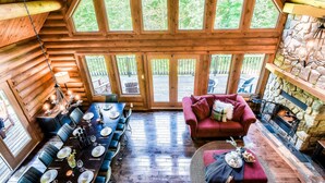 L’intérieur d’une cabane en rondins comprend un coin repas, une cheminée et de grandes fenêtres.