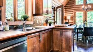 Une cuisine rustique aménagée dans une cabane en rondins, avec des meubles de rangement en bois, un évier et un coin repas comprenant une table et des chaises.