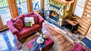 L’intérieur chaleureux d’un chalet en bois, avec une cheminée en pierre, un canapé rouge et un coin repas où se trouve un plateau de nourriture.