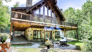 Une cabane en rondins avec des fondations en pierre, une terrasse en bois et un espace aménagé pour faire un feu de camp.