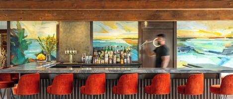 Eine Bar mit Holzbalkendecke, roten Barhocker, einer Auswahl an Flaschen und einem großen abstrakten Gemälde an der Wand.