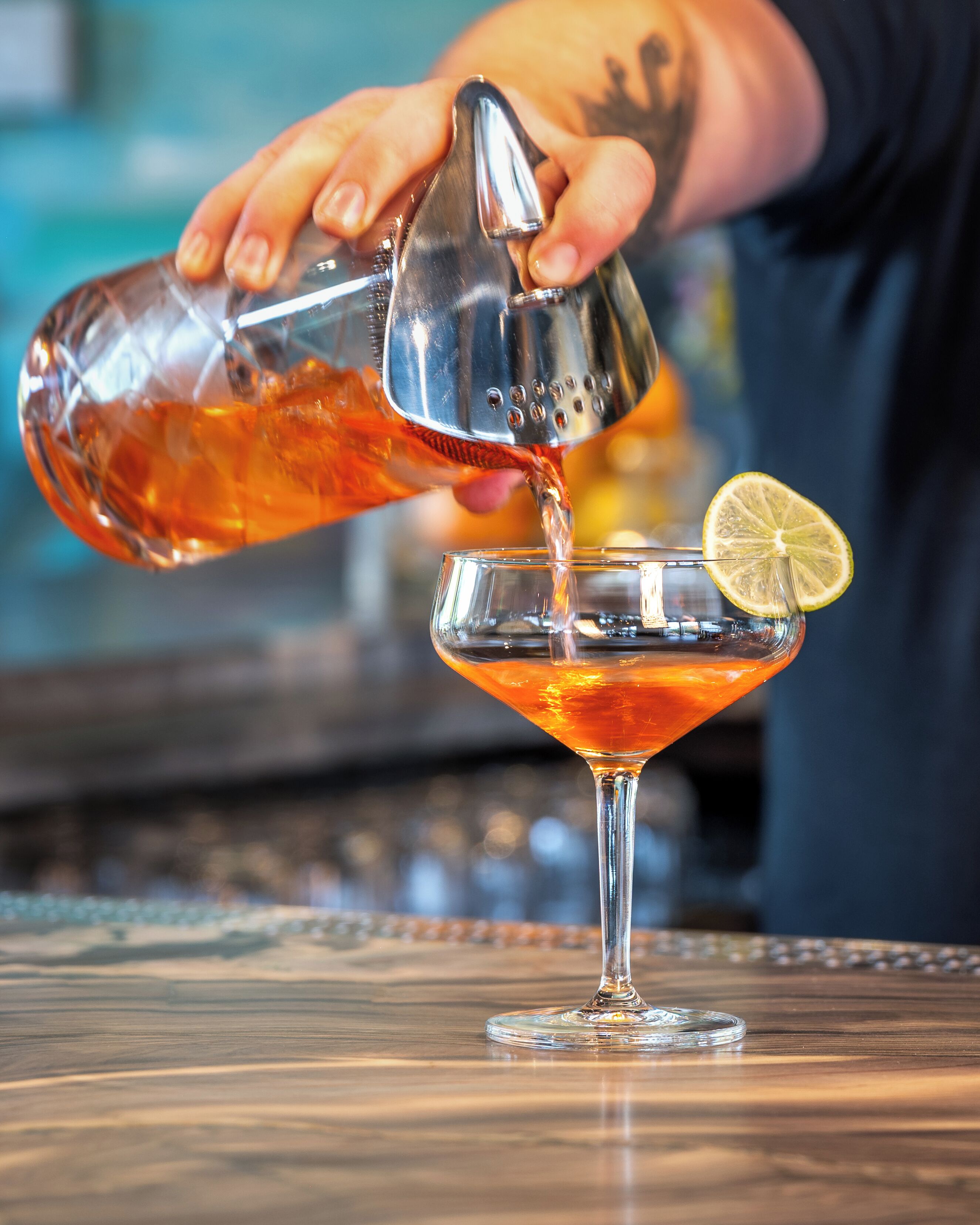 A person pouring a drink into a martini glass with a lemon slice on the rim.