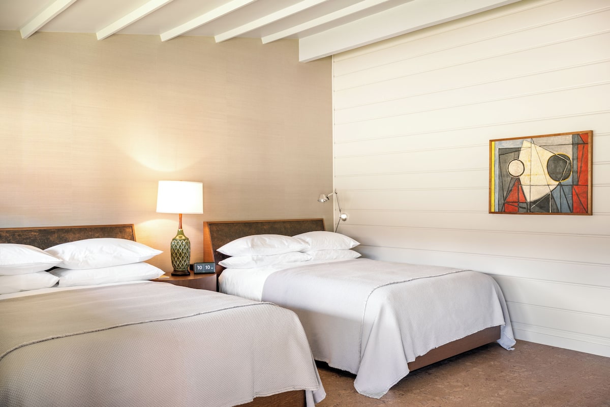 A hotel room with two beds, a nightstand with a lamp, and a painting on the wall.