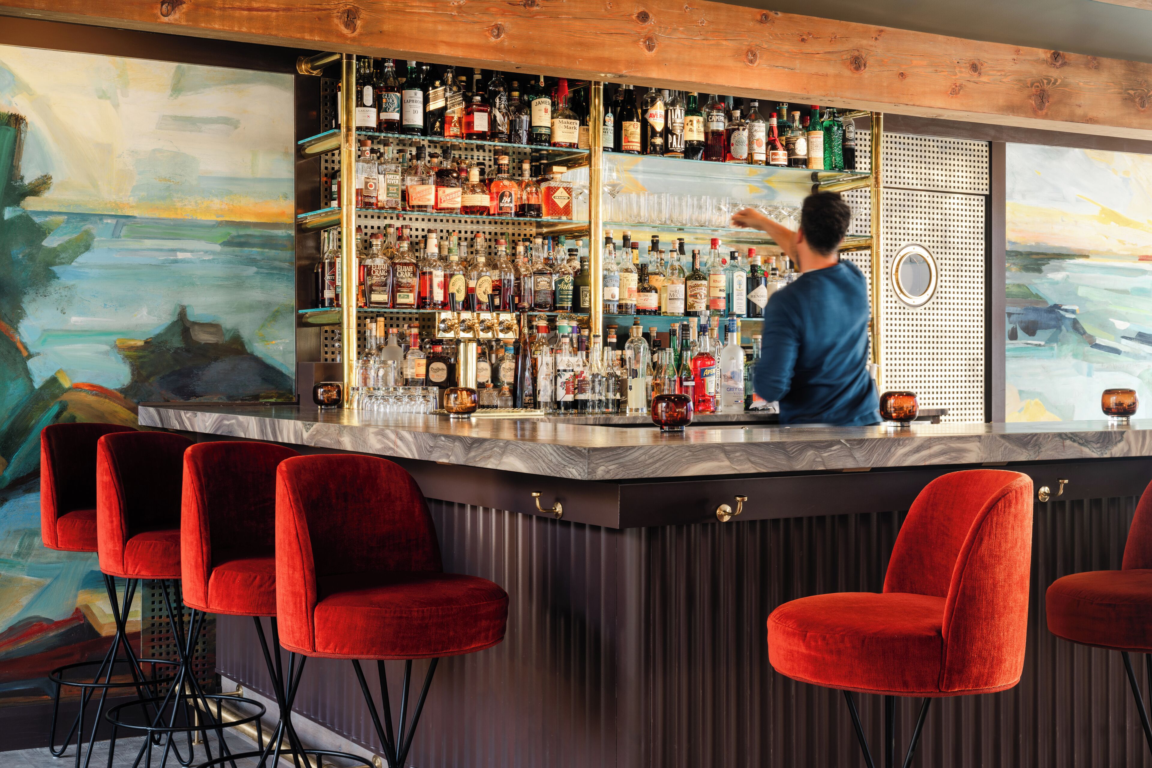 A bar area with a bartender, red bar stools, and a wall of liquor bottles.