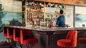 A bar area with a bartender, red bar stools, and a wall of liquor bottles.