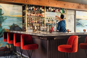 A bar area with a bartender, red bar stools, and a wall of liquor bottles.