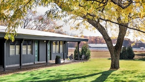 Un bâtiment moderne doté d’un patio couvert, d’une pelouse et d’un grand arbre aux feuilles jaunes.