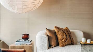 Un salon moderne avec un canapé gris clair, un fauteuil marron et une table d’appoint en bois sur laquelle sont posés des livres et un bol décoratif.