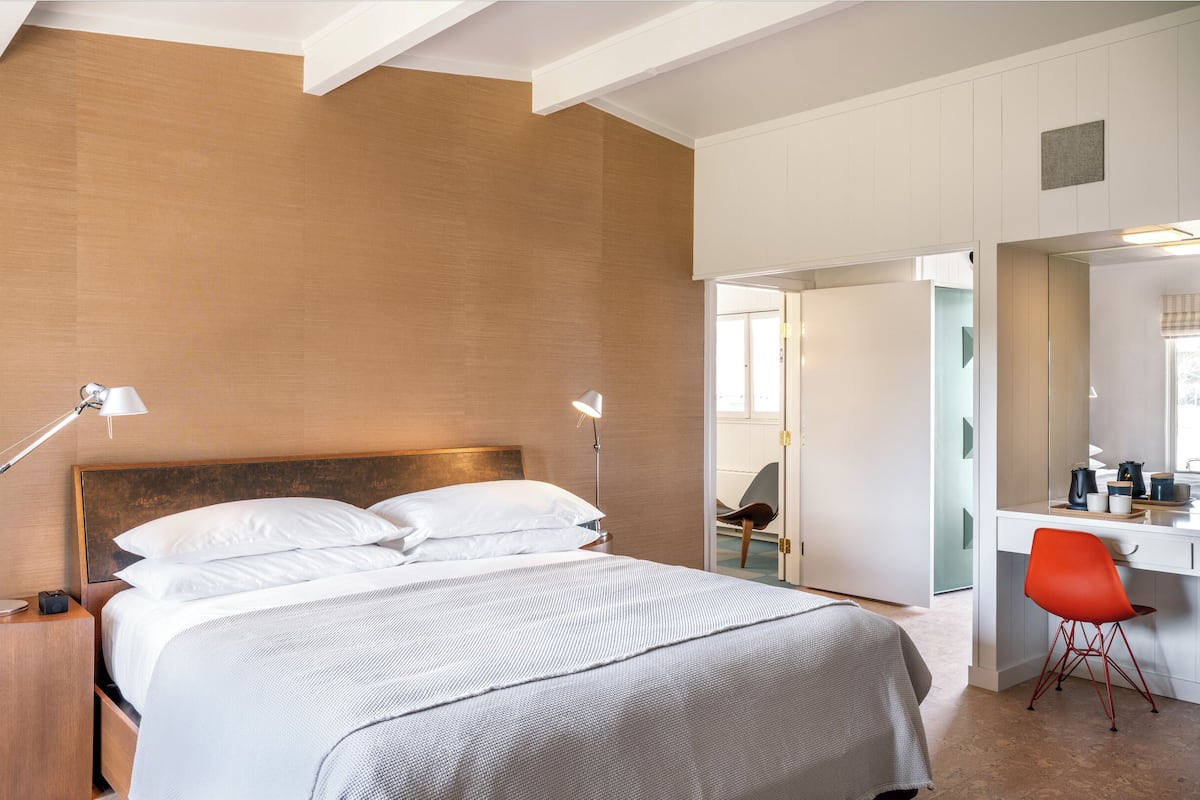 A hotel room with a large bed, bedside lamps, a desk with a chair, and a bathroom visible through an open door.