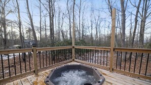 Un jacuzzi en una terraza de madera con barandilla de metal, rodeado de árboles.