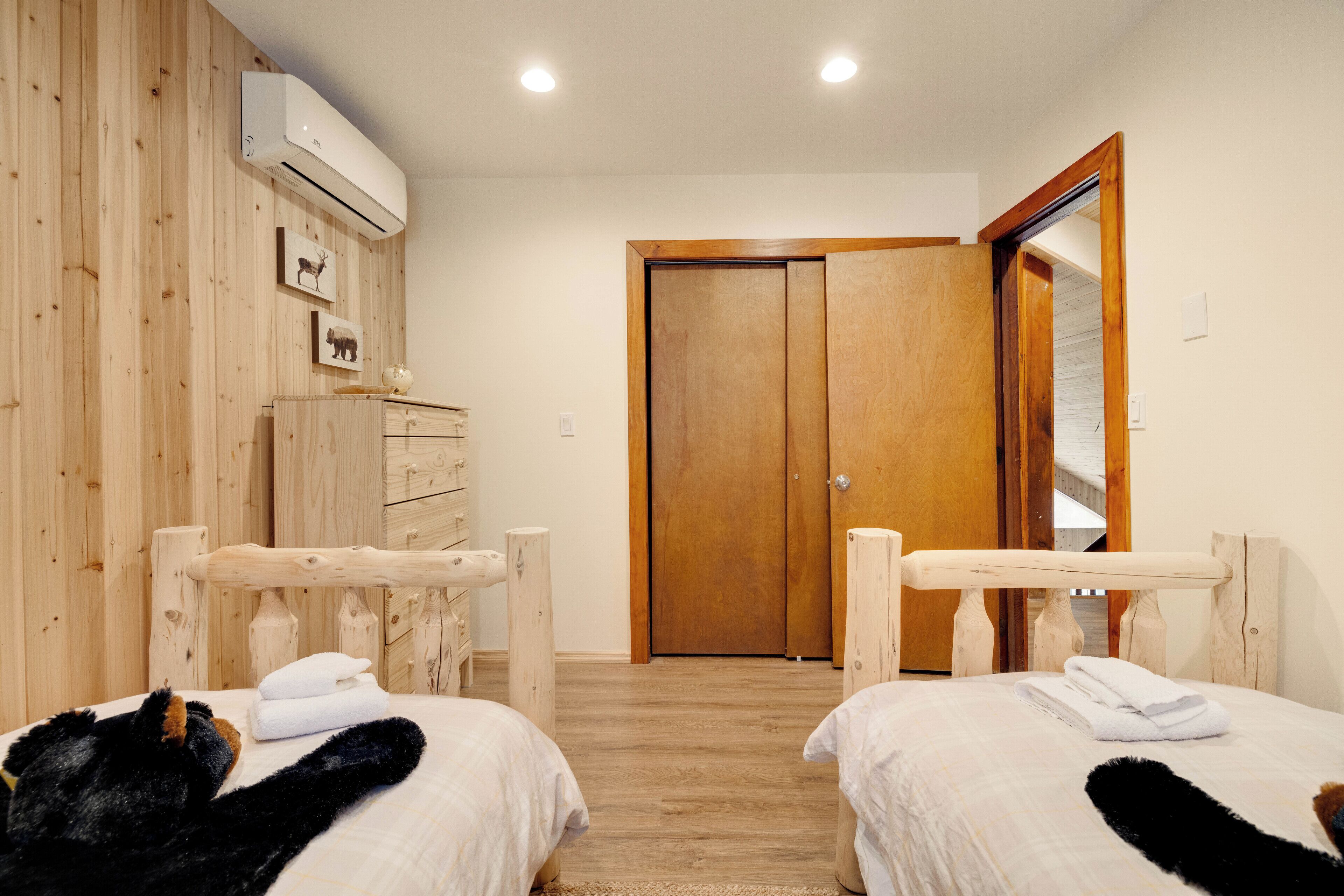 A hotel room with two beds, wooden walls, a wooden door, and an air conditioning unit.