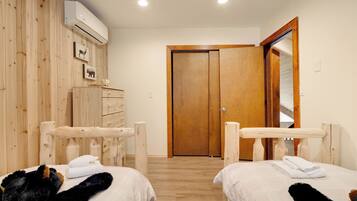 A hotel room with two beds, wooden walls, a wooden door, and an air conditioning unit.