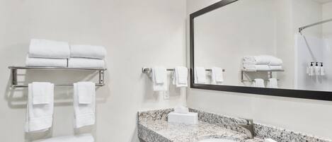 A modern bathroom with a toilet, sink, and large mirror. There are multiple towels on racks and a shower area visible in the mirror reflection.