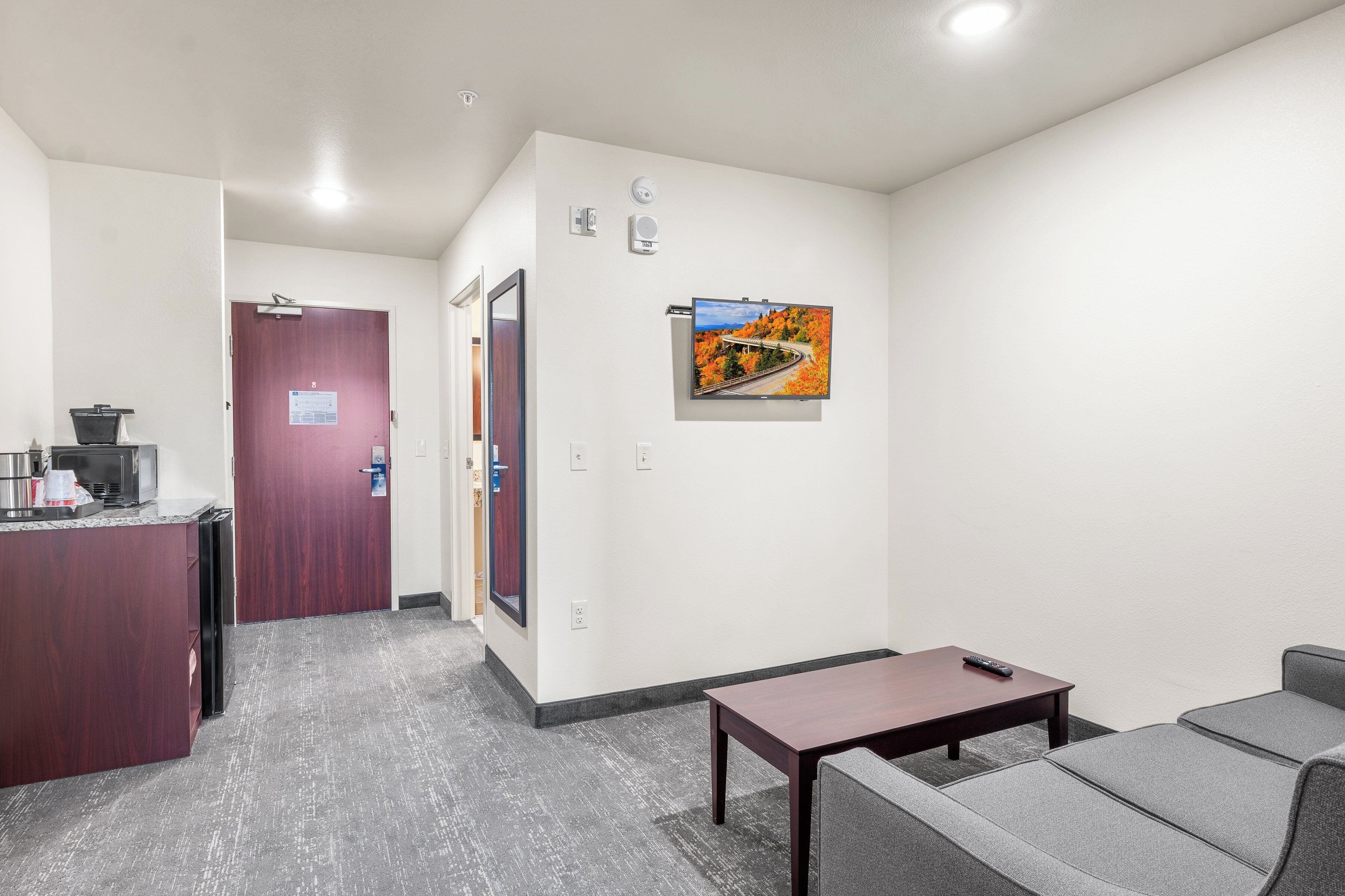 A hotel lobby with a reception desk, a seating area with a table and chairs, and a wall-mounted television.