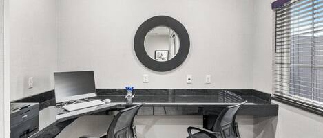 A modern office space with a large desk, two office chairs, a desktop computer, a printer, and a mirror on the wall.