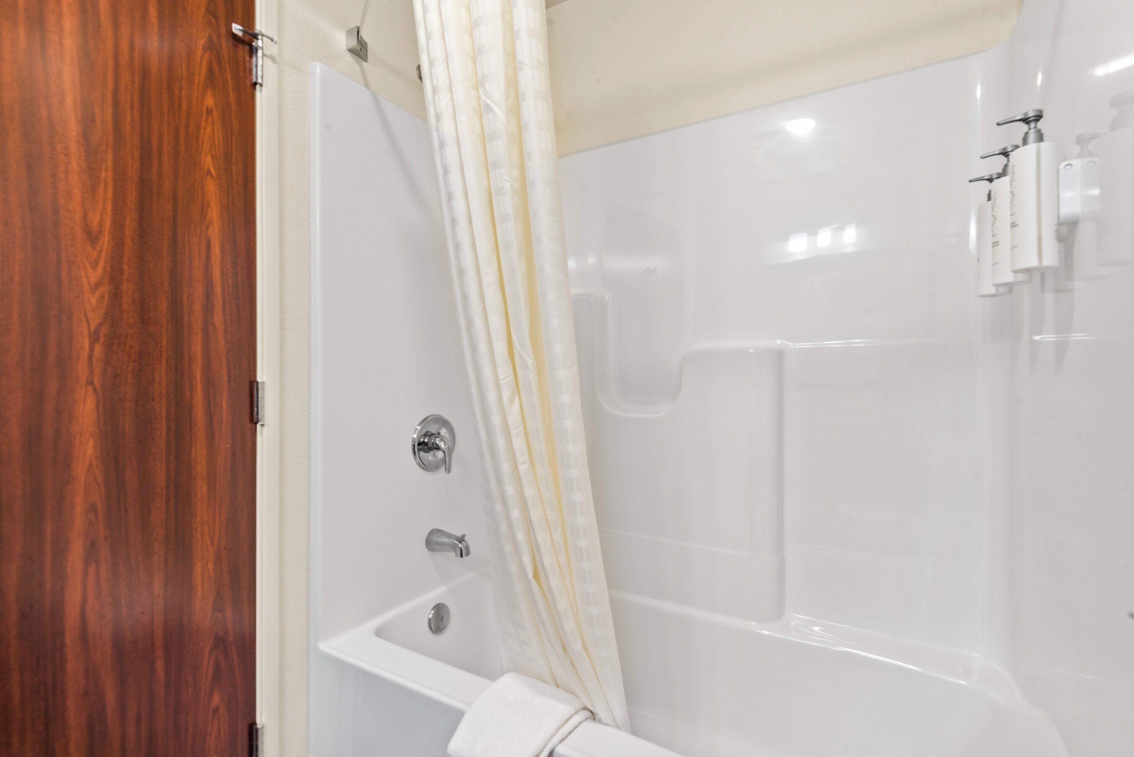 A bathroom with a wooden door, a bathtub, a shower curtain, and a towel rack.