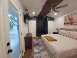 Une chambre à coucher avec un lit, un bureau, une chaise, un ventilateur de plafond et un tableau accroché au mur.