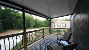 A covered porch with a patterned rug, two chairs, and a view of a road and trees. - Cozy 1-bdrm/1 bath, desk, grill, deck, laundry (Phenix City)