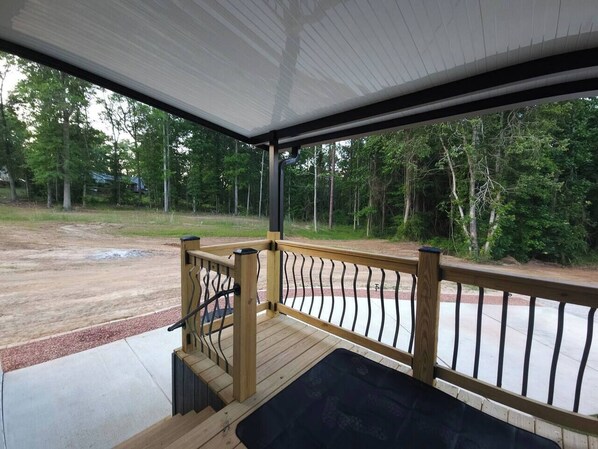 A covered outdoor area with a wooden deck, metal railing, and a view of a forested area.