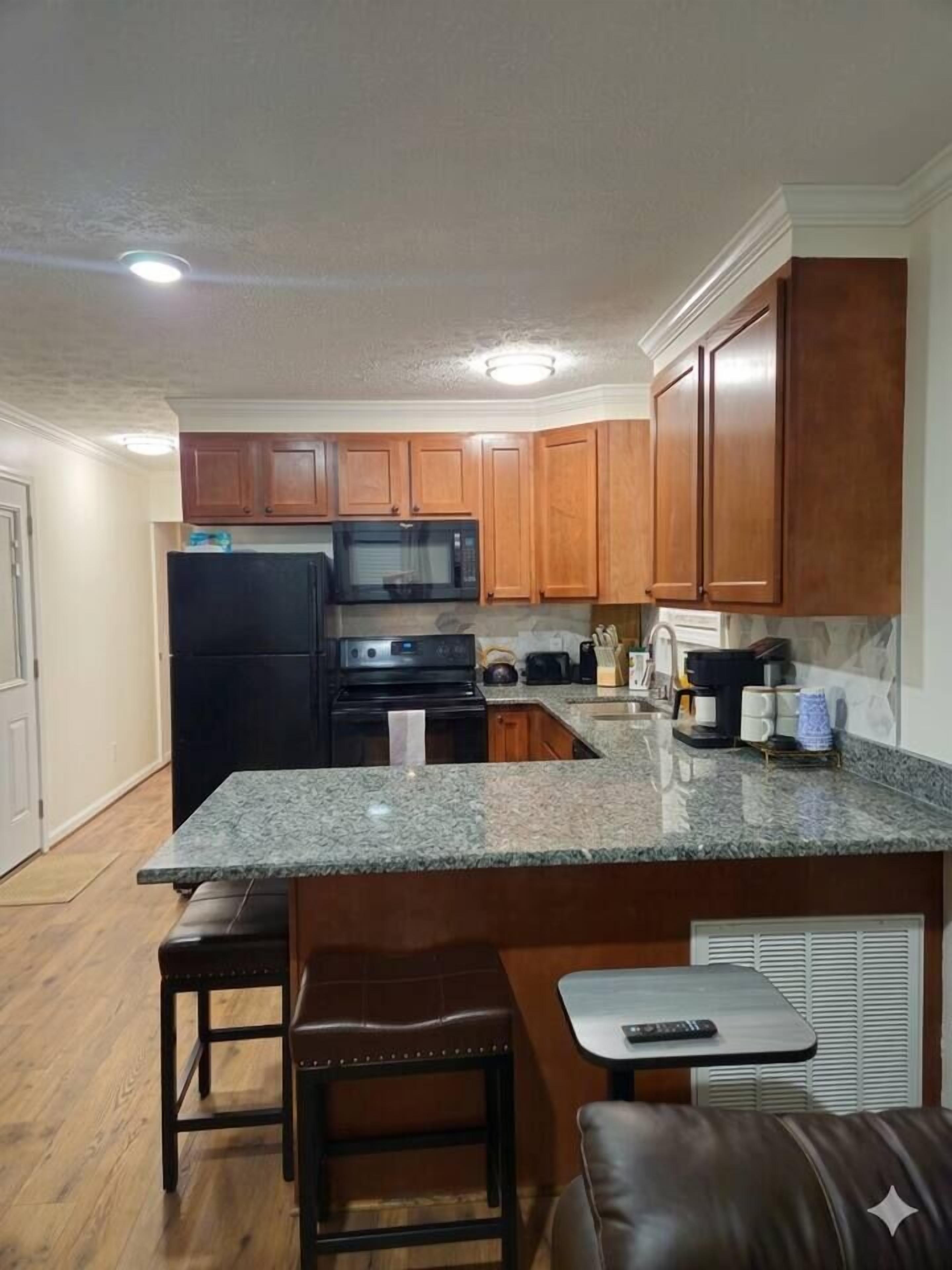 A kitchen with wooden cabinets, a black refrigerator, a microwave, a stove, and a granite countertop.