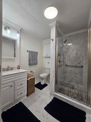 Une salle de bain avec un meuble-lavabo blanc, des toilettes, une douche avec une porte en verre et un sol en marbre.