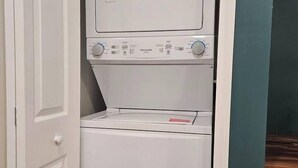 A compact, white laundry room with a front-loading washer and dryer, a door, and a green wall. - Cozy 1-bdrm/1 bath, desk, grill, deck, laundry (Phenix City)