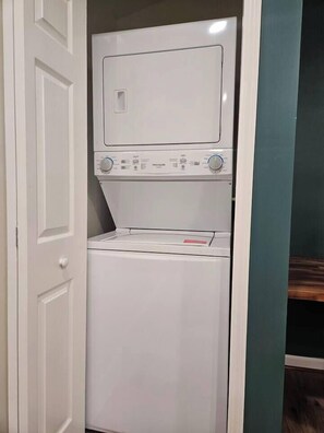 A compact, white laundry room with a front-loading washer and dryer, a door, and a green wall. - Cozy 1-bdrm/1 bath, desk, grill, deck, laundry (Phenix City)