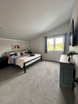 Un dormitorio con cama, mesita de noche, cómoda, ventana con cortinas y un cuadro en la pared.