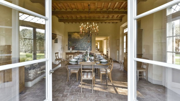 Un espace repas avec une grande table dressée pour accueillir plusieurs personnes, des chaises en bois et un lustre.