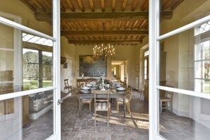 Een eethoek met een grote tafel voor meerdere personen, houten stoelen en een kroonluchter.