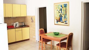 Eine kleine Küche mit gelben Schränken, einem Esstisch mit zwei Stühlen und einem Bild an der Wand.