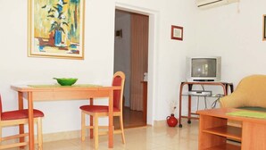 Ein Wohnzimmer mit einem Holzesstisch, zwei roten Stühlen, einem Fernsehgerät auf einem Schrank und einem Gemälde an der Wand.