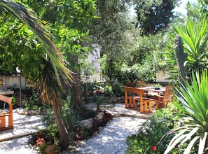Un patio ajardinado con suelo de piedra, muebles de madera y diversas plantas.
