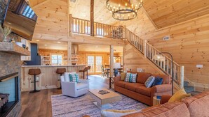 A spacious living area with a fireplace, a staircase, and a kitchen in a wooden cabin. - Moksha Retreat - A-Frame|Mtn Views|Hot Tub|King Ensuites (Black Mountain)