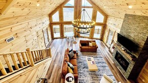 A spacious wooden cabin with a high ceiling, a large living area with a sofa and fireplace, and a staircase leading to an upper level. - Moksha Retreat - A-Frame|Mtn Views|Hot Tub|King Ensuites (Black Mountain)