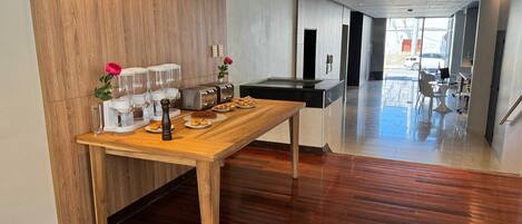 A modern kitchen with wooden flooring, a wooden table with breakfast items, and a view of the outside.